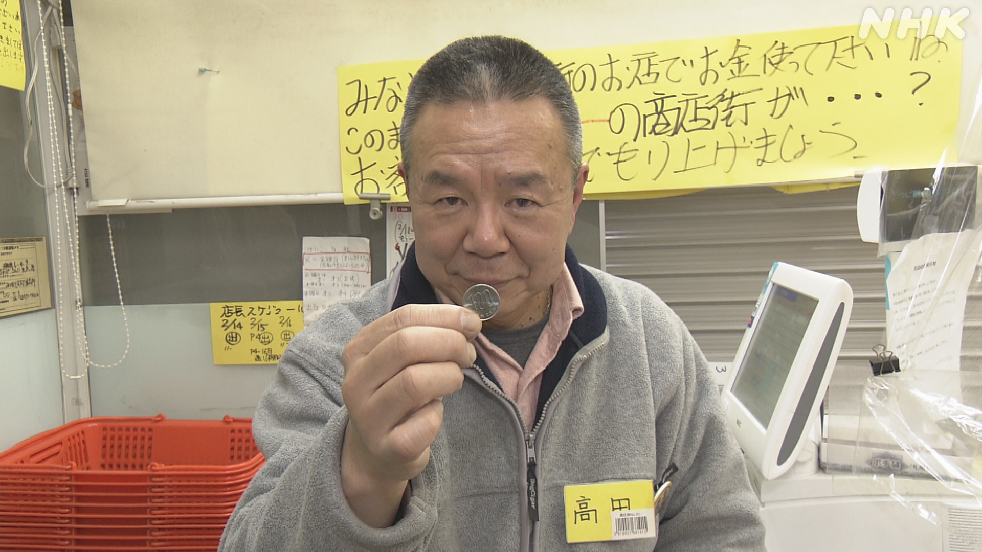 100円玉を手にポーズをとる、店長の高田さん